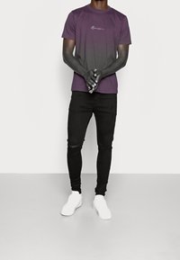 Tričko s krátkým rukávem v odstínu přecházejícím z fialové do šedé, s bílým logem, doplněné o černé úzké džíny a bílé tenisky.