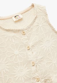 Beige striktop med blomsterdesign, rund halsudskæring, fem små knapper og tekstil med hævede blomstermotiver.