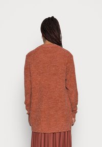 Maglione oversize a maniche lunghe in tessuto lavorato arancione ruggine, con scollatura tonda e polsini a coste, dalla finitura morbida e testurizzata.