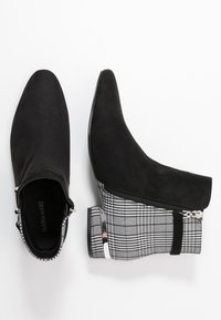 Černé semišové kotníkové boty s špičatou špičkou, které mají kostkovaný textilní vzor a zipový uzávěr. Obsahují kovový akcent na podpatku.