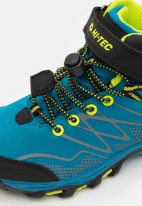 Blue hiking shoe with black accents and gray design elements. Features a textured sole, yellow eyelets, and integrated tightening mechanism.