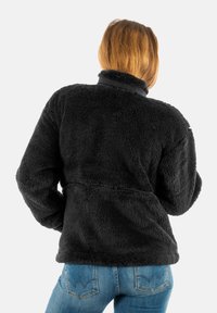 Sudadera de forro polar negra con un cuello alto y un acabado texturado y esponjoso. Presenta una costura horizontal y un corte relajado. Llevada con jeans azules.