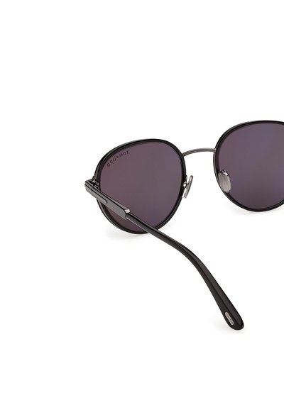 Černé sluneční brýle s kovovým rámem, tmavými kulatými čočkami, nastavitelnými nosními polštářky a tenkým zakřiveným ramenem směřujícím vpřed.