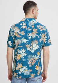 Chemise à manches courtes bleue avec des motifs de feuilles tropicales colorées. Fabriquée en matériau léger, dotée d'un col classique et d'une coupe décontractée.