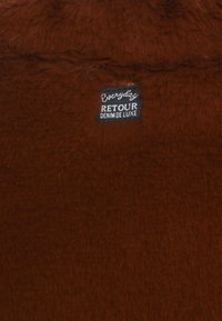 Brunt, pälsliknande tyg med en texturerad yta. Etiketter visar "Everyday" och "Retour Denim De Luxe" i svart och vitt.
