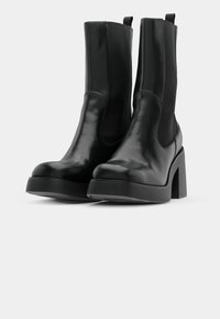 Black ankle boots featuring a smooth leather exterior, elastic side panels, block heels, and a rounded toe. Textured fabric accents on sides.