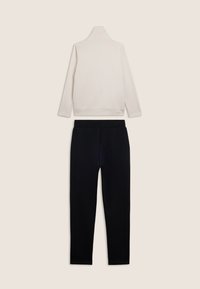 Maglione bianco a maniche lunghe con collo a dolcevita e pantaloni neri slim-fit disposti su uno sfondo chiaro, mostrati dal retro.