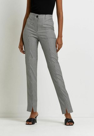 Mujer con pantalones de cintura alta a cuadros en blanco y negro con aberturas frontales, camiseta negra sin mangas y sandalias negras de tacón con dedos abiertos.