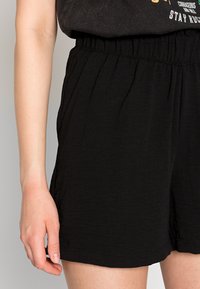 Zwarte shorts met een elastische tailleband en textuurstof, voorzien van zijzakken en een ontspannen pasvorm, die tot halverwege de dij reiken.