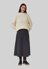 Cremefarbener gestrickter Pullover mit weiten Ärmeln, kombiniert mit einem langen dunkelgrauen Rock und klobigen schwarzen Stiefeln mit einer strukturierten Akzentuierung.