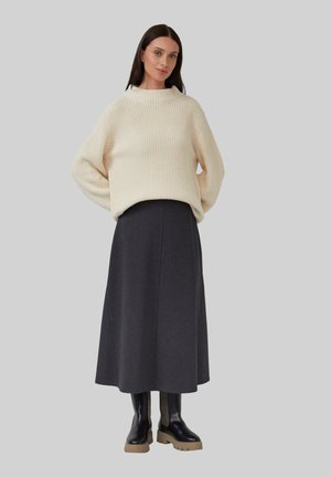 Pull en tricot beige avec des manches larges, associé à une longue jupe gris foncé et des bottes noires massives avec une touche texturée.