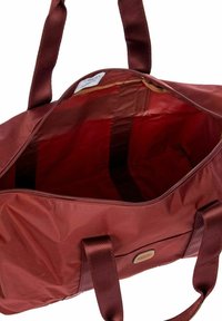 Borsa a duffel in nylon color bordeaux con chiusura a zip e manici in tessuto. Interno foderato di una tonalità più chiara con una tasca.