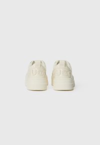 Cream-colored sneakers with a textured rubber sole, embossed "HUGO" branding on the heel, and a rounded design featuring pull tabs.