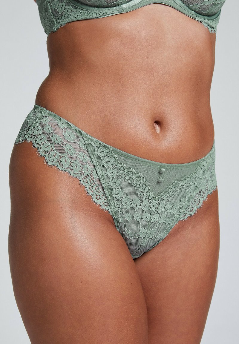 Groene kanten slipjes met bloemmotieven, doorschijnende stof en gegolfde randen. Twee decoratieve knopen aan de voorkant voegen detail toe.