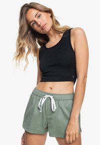 Top corto negro de tejido texturizado, combinado con pantalones cortos de algodón verdes con cordón y aberturas laterales.
