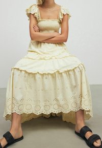 Robe longue et échelonnée de couleur jaune clair avec un décolleté carré. Elle possède des manches volantées et un riche détail en oeillets à l'ourlet.