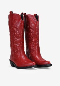 Botas de vaquero de cuero rojo con un intrincado bordado, punta afilada y un tacón bajo. Presentan patrones decorativos en el caña y una textura suave.