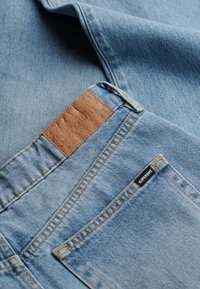 Jeansy z dżinsu w jasnoniebieskim odcieniu z brązową skórzaną naszywką z wypukłym wzorem, kontrastującym żółtym szwem i czarną etykietą marki.