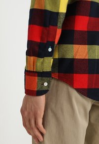 Camicia di flanella con un motivo a quadri multicolori nei toni di rosso, arancione, giallo e verde. Caratterizzata da un polsino con bottoni e una texture morbida.