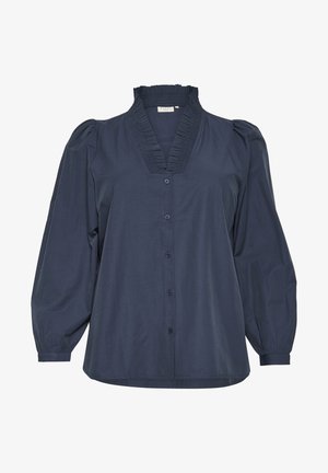 Tumedan sinine nööbitav pluus volangkaelusega, pleatitud kaelaosaga ja puhvis varrukatega. Valmistatud siledast kangast, millel on vabalt langev lõige.