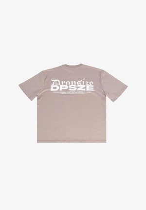 Beige cotton t-shirt, short sleeves, crew neck. Back features large white graphic text and brand accents. Smooth texture, casual design.