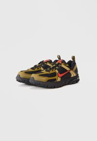 Tênis de corrida Nike nas cores preto e verde-azeitona com o logótipo swoosh vermelho, solas pretas, detalhes em malha e laços de puxar no calcanhar, sobre fundo branco.