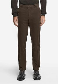 Bruna skräddarsydda byxor i slät tyg med något avsmalnande ben, med bälte och sidofickor, ihop med svarta kostymskor.