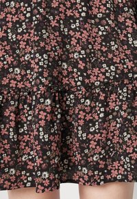 El vestido negro con flores presenta flores en tonos rosa, blanco y púrpura, una tela texturizada y un dobladillo con volantes.