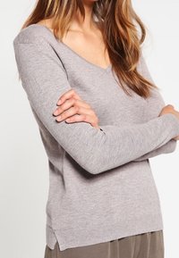 Hellgrauer Strickpullover mit V-Ausschnitt und langen Ärmeln, ausgestattet mit gerippten Bündchen und Saum sowie seitlichen Schlitzen für mehr Bewegungsfreiheit.