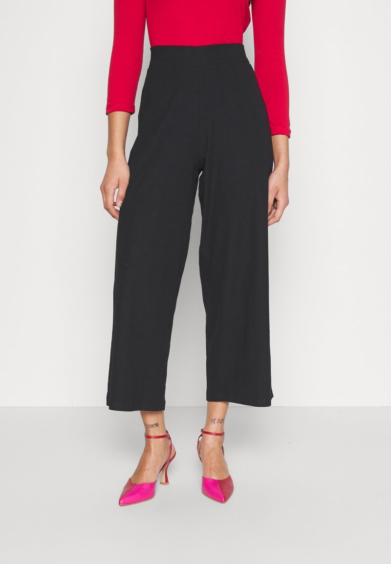 Černé široké nohavice s vysokým pasem, vyrobené z jemné látky, v kombinaci s jasně růžovými špičatými podpatky. Minimalistický design, bez vzorů.