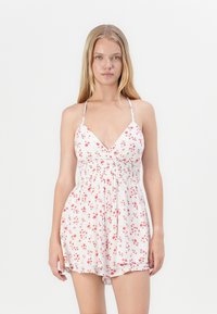 Romper blanco con flores que presenta un escote en V, tirantes finos ajustables y patrones florales rojos. Material texturizado y ligero con cintura elástica.
