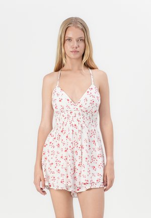 White floral romper featuring a V-neckline, adjustable spaghetti straps, and red floral patterns. Textured, lightweight material with elastic waist.