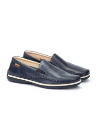 Zapatos slip-on de cuero azul marino con un detalle de costura en la parte superior, paneles laterales elásticos y suela de goma. El interior es beige.