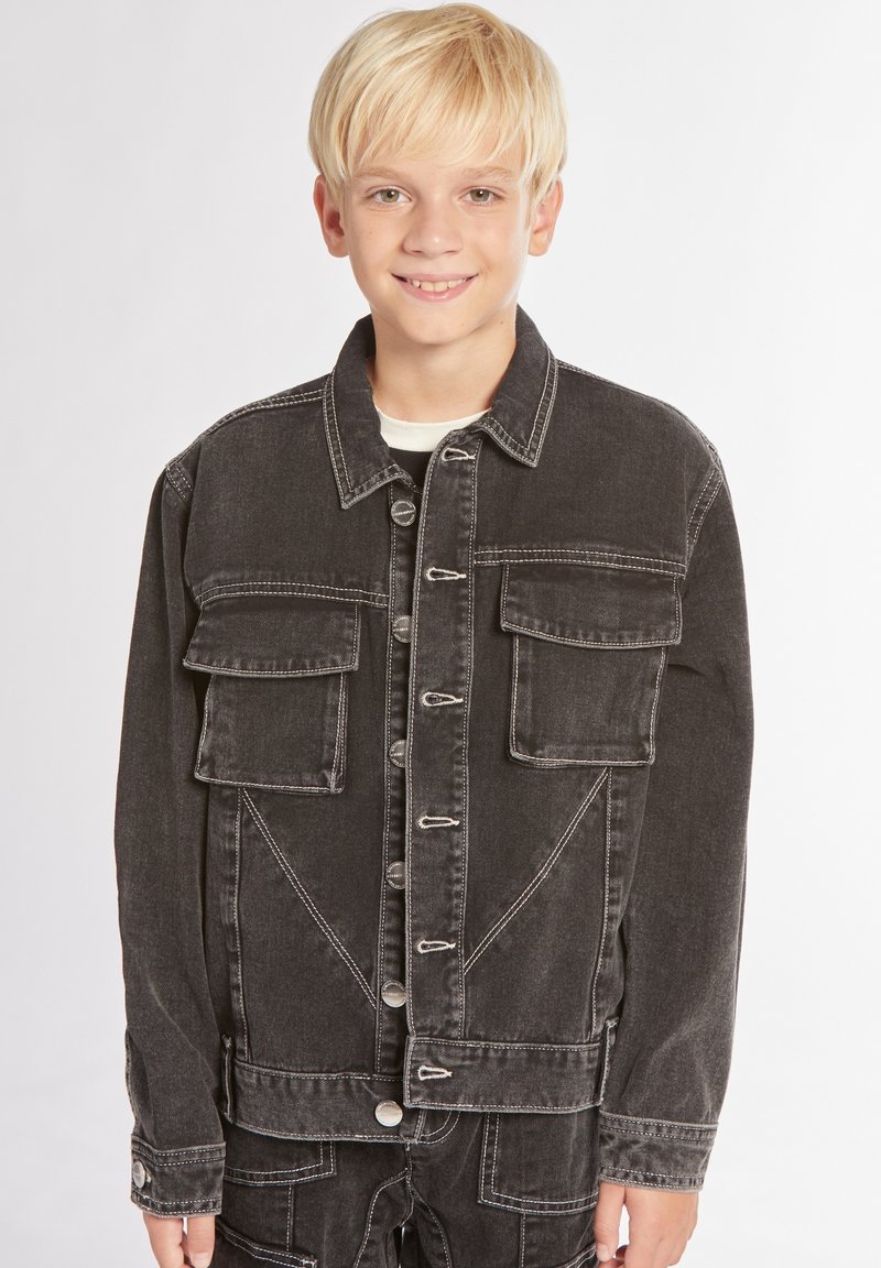 Giubbotto in denim nero con due tasche sul petto, bottoni metallici e dettagli di cucitura bianca. Presenta una vestibilità dritta e maniche lunghe.