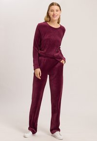 Conjunto de loungewear burdeos hecho de tejido suave; camiseta de manga larga con un escote amplio, combinada con pantalones de corte relajado que cuentan con bolsillos.