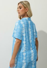 Maglietta azzurra con tie-dye realizzata in tessuto a costine, con colletto, caratterizzata da tonalità variabili di blu e bianco, maniche corte e una vestibilità ampia.