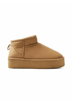 Bottines en daim tan avec un bout arrondi, un col bas et une semelle en caoutchouc épaisse avec un bord texturé. Tirant à l'arrière pour un enfilage facile.