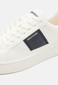 Weiße Sneaker aus glattem Leder, mit einem navyblauen Akzentpatch, einer strukturierten Gummisohle und flachen Baumwollschnürsenkeln mit Logo-Detaillierung.