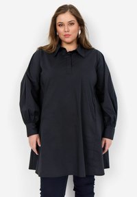 Camicia tunica nera con colletto, abbottonatura e maniche lunghe a sbuffo. Realizzata in tessuto morbido con una vestibilità comoda e tasche laterali.