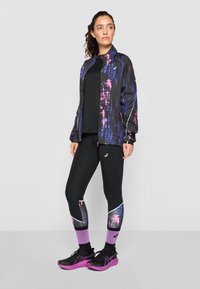 Veste de sport noire avec un motif abstrait violet et rose, associée à des leggings noirs présentant un accent coloré, et des chaussures de course noires avec des détails violets.