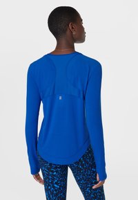 Blauwe lange mouwen sporttop met een gestructureerde achterkant en een ronde zoom. Soepele stof met een aansluitend ontwerp, gecombineerd met een patroonlegging.