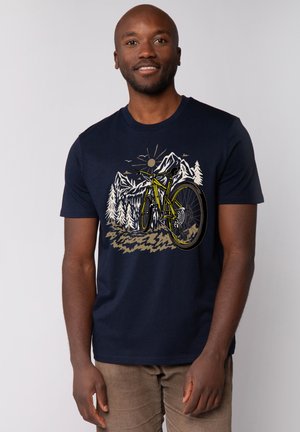 Marineblauwe katoenen t-shirt met een grafisch ontwerp van een gele mountainbike, omringd door bomen en bergen, met details in wit, bruin en geel.
