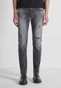 Vaqueros de denim gris deslavado con detalles desgastados, diseño clásico de cinco bolsillos, corte recto, combinados con botas negras hasta el tobillo.