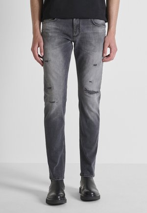 Jeans en denim gris délavé avec des détails déchirés, design classique à cinq poches, coupe droite, associés à des bottes noires à la cheville.