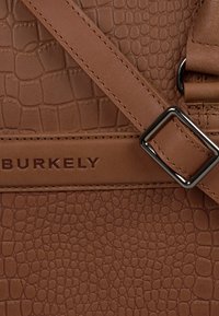 Brązowa torba skórzana z fakturą i wytłaczanym wzorem, regulowanym paskiem, metalowym zapięciem oraz nazwą marki "BURKELY" z przodu.