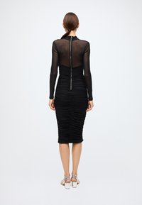 Black midi dress with a fitted silhouette, sheer long sleeves, and ruched detailing. Features a back zipper for closure.
