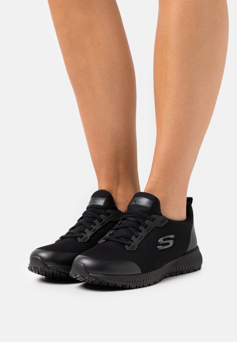 Schwarze Sportschuhe mit einem Obermaterial aus Mesh, einer strukturierten Gummisohle und tonal abgestimmtem Branding an der Seite und der Zunge. Sie verfügen über Schnürsenkel und ein rutschfestes Design.