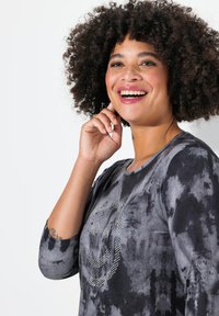 Schwarz- und graues Batik-Langarmshirt mit Rundhalsausschnitt, das auf der Vorderseite mit einem Strass-Lächelgesicht-Design versehen ist. Weiche Textur.
