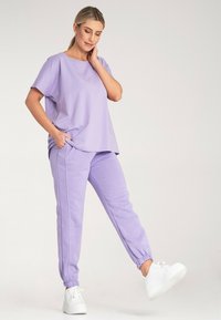 Liliowa bluzka z krótkim rękawem i dopasowane joggery wykonane z miękkiego materiału; spodnie mają elastyczne mankiety i boczne kieszenie, dopełnione białymi sneakersami.