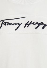 Biały bawełniany sweter z teksturowanym wzorem i poziomym pasem. Wyrazisty czarny haftowany logo "Tommy Hilfiger" na klatce piersiowej.